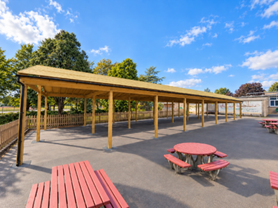 Large timber canopy with black guttering in playground with red benches